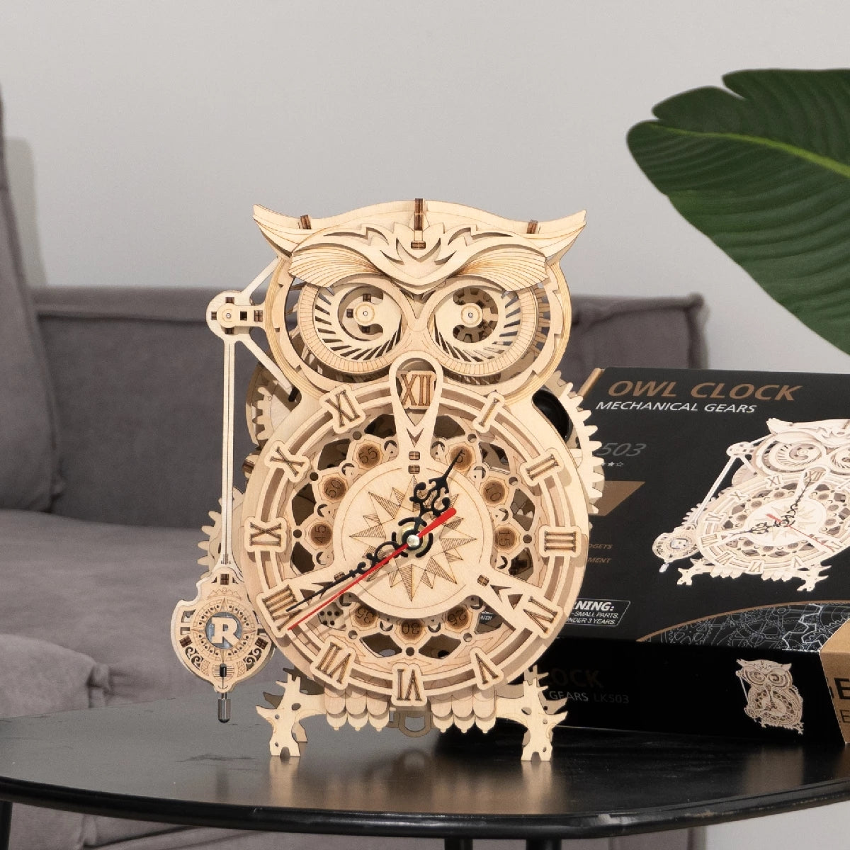 Wooden owl clock with mechanical gears on a table, box in the background