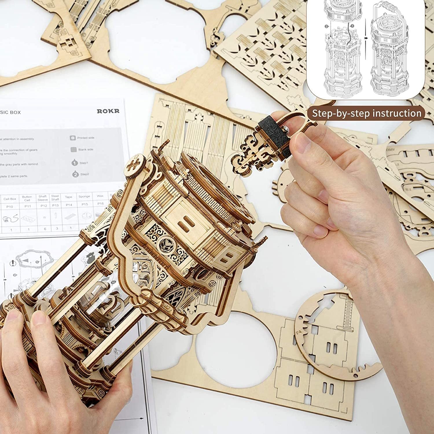 Wooden mechanical model kit with hands assembling it, step-by-step instructions visible.